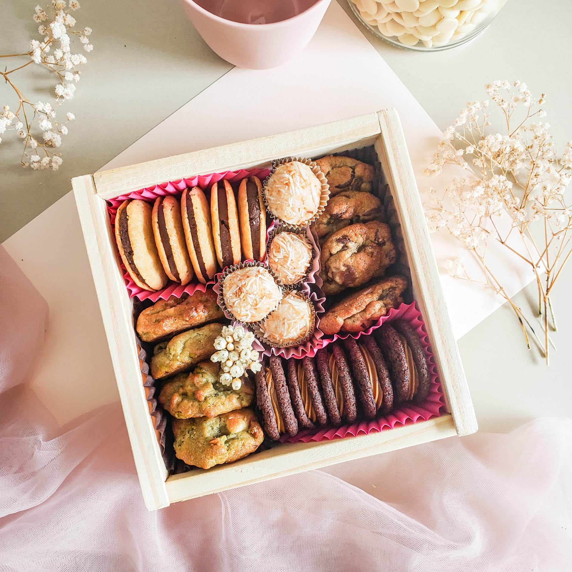 Caixa Petit Delicadezas aberta, vista de cima, com cookies, alfajores e brigadeiros em forminhas rosas